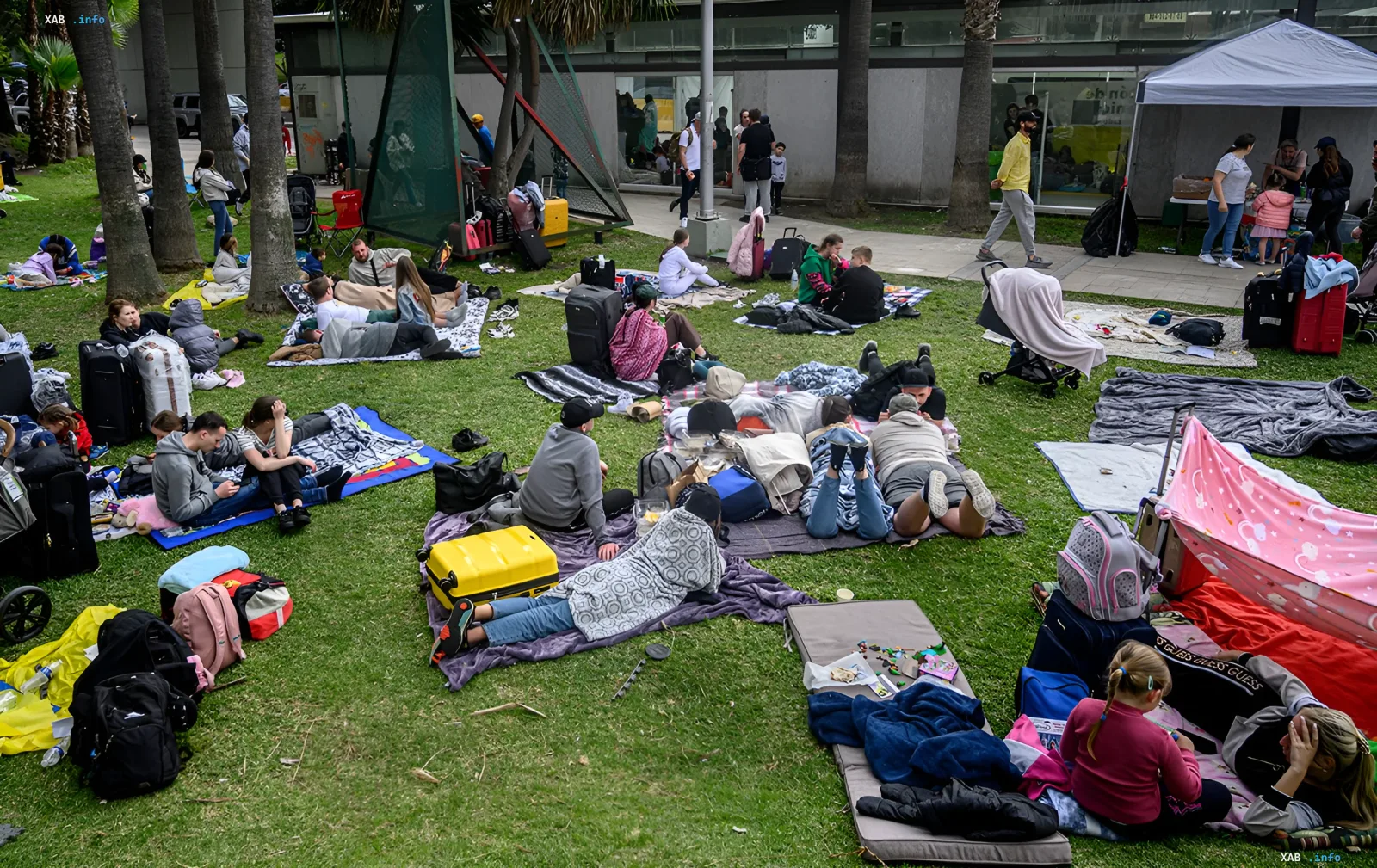Ukrainian refugees rest on grass with suitcases awaiting US court decision on work visas