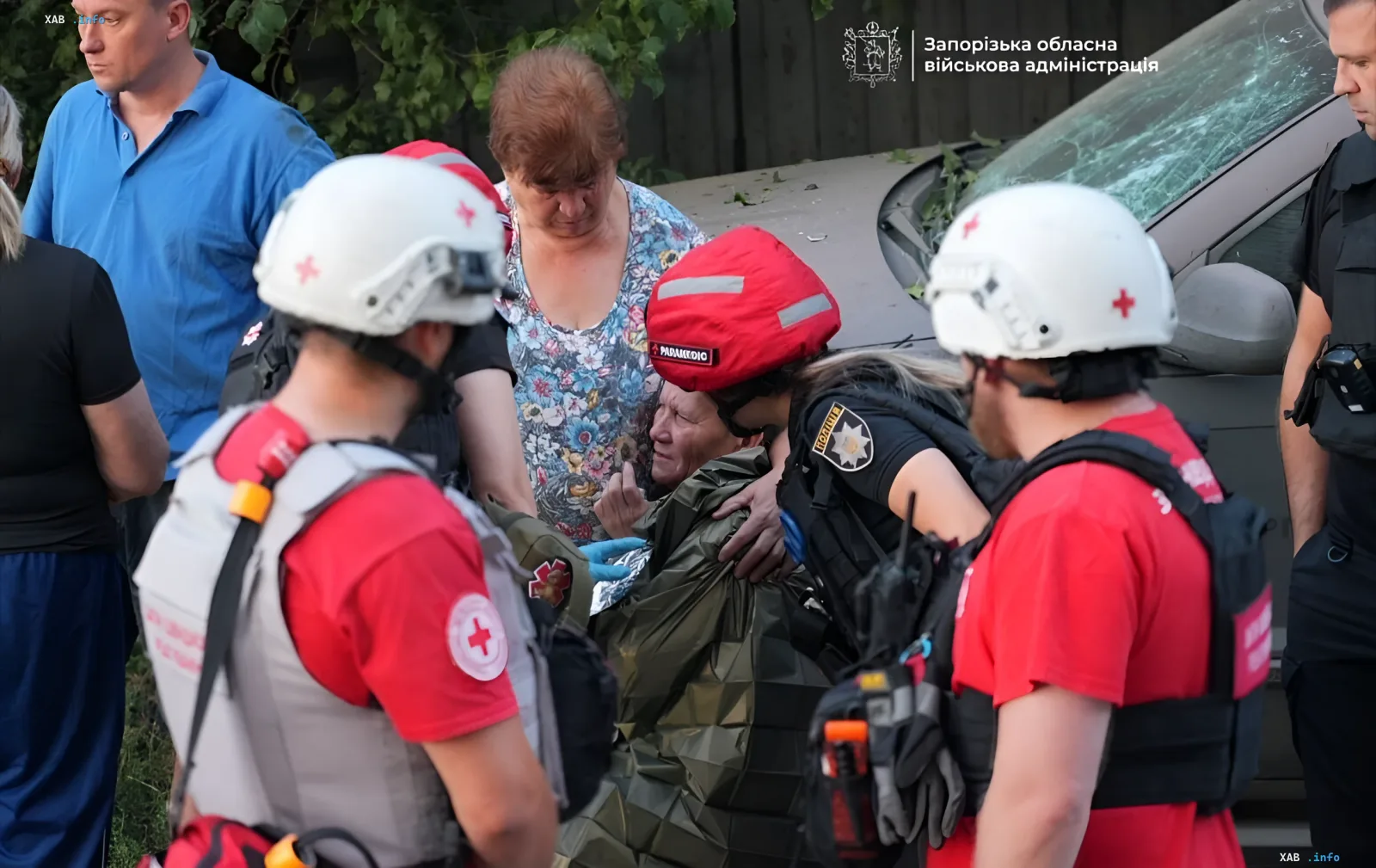 Медики спасают пострадавшую женщину после российского удара в Запорожье, рядом разбитая машина и волонтеры