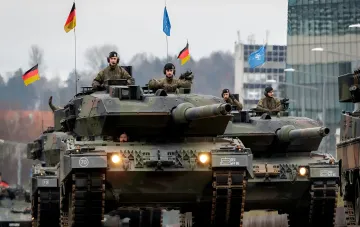Немецкие танки Leopard 2A7 с флагами Германии и НАТО на учениях, иллюстрирующие сокращение закупок боеприпасов Rheinmetall в 2027 году