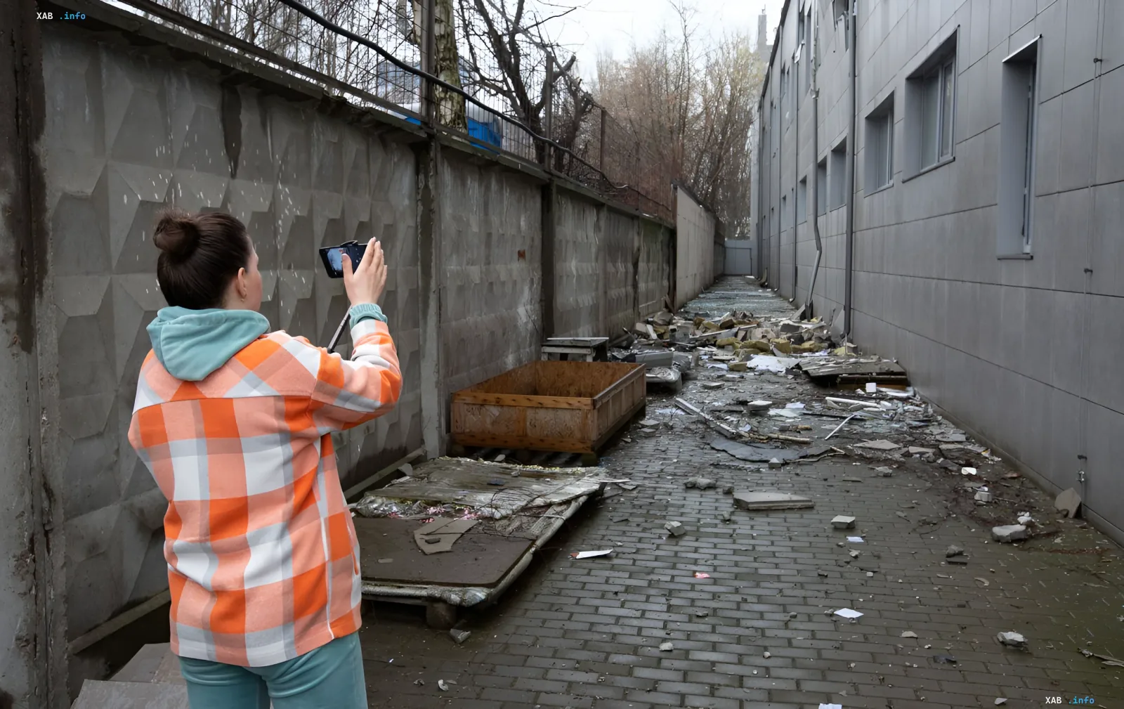 Женщина фотографирует последствия обстрела в узком проходе между зданиями в Киеве, фиксируя разрушения для реестра