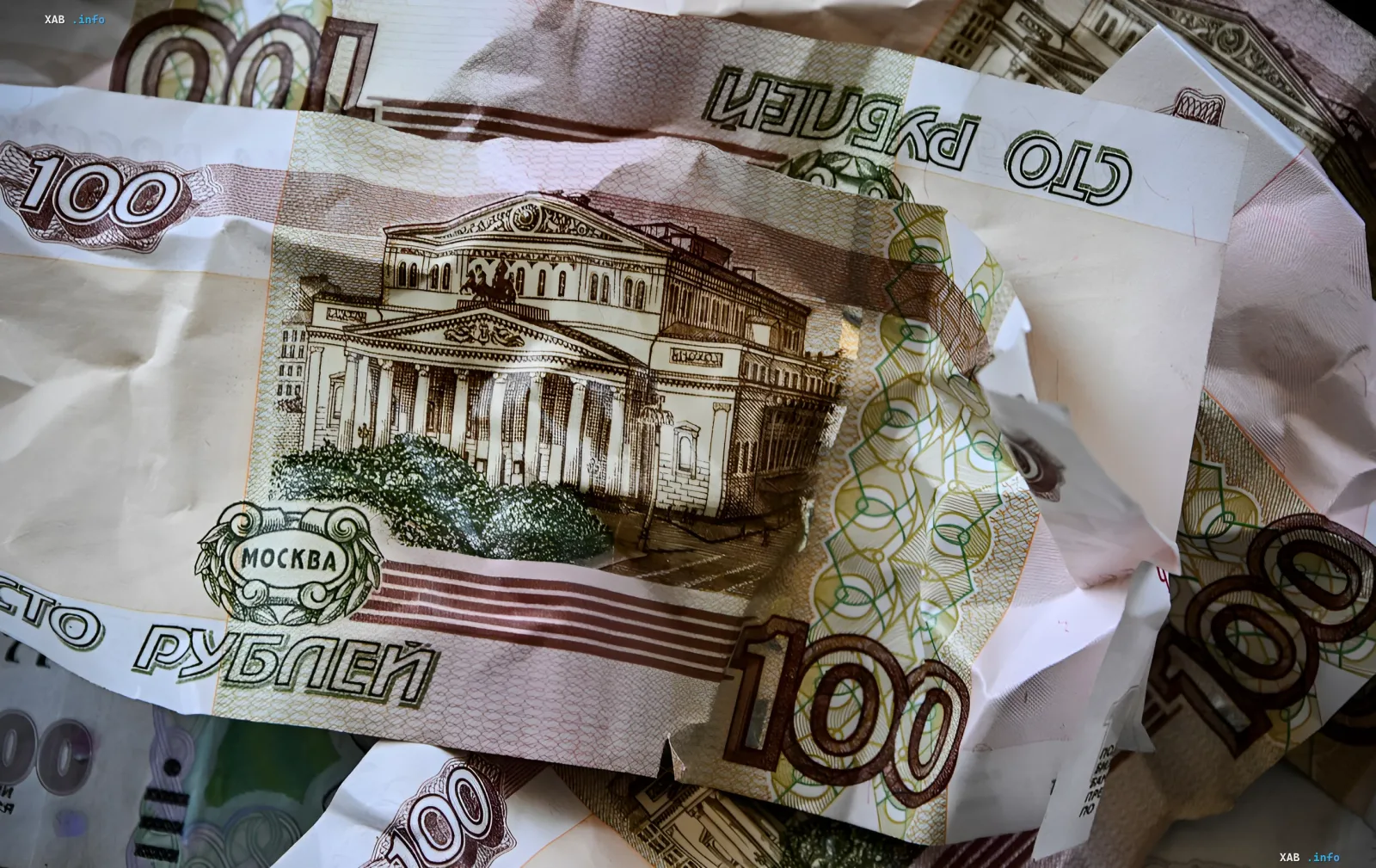 Смятые купюры российских рублей номиналом 100 рублей, символизирующие инфляцию и скрытую эмиссию для финансирования войны через принудительную покупку облигаций.