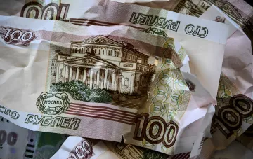 Смятые купюры российских рублей номиналом 100 рублей, символизирующие инфляцию и скрытую эмиссию для финансирования войны через принудительную покупку облигаций.