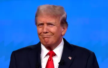 Дональд Трамп в деловом костюме с американским флагом на лацкане, улыбаясь на фоне синего экрана — иллюстрация к статье о смене курса Трампа в поддержке Зеленского