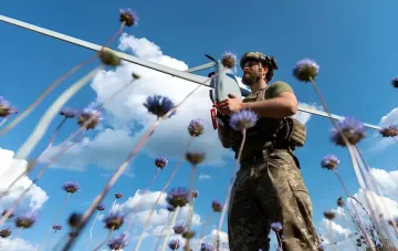 Украинский военнослужащий с беспилотным летательным аппаратом на фоне полевых цветов и голубого неба