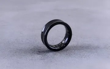Черное умное кольцо Apple Ring с видимой внутренней электроникой на сером фоне, иллюстрирующее новый патент на универсальный пульт для экосистемы