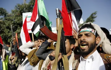 Houthi fighters with weapons and Iraqi flags at a demonstration, illustrating the topic of a new trade tax through the Red Sea