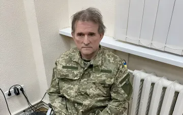 Владимир Медведчук в военной форме с украинским флагом на рукаве, сидящий в помещении, в контексте нового дела против него