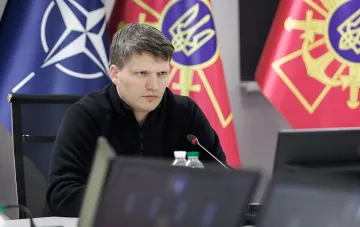 Новый замминистра обороны Украины за столом переговоров с флагами НАТО и Украины на фоне