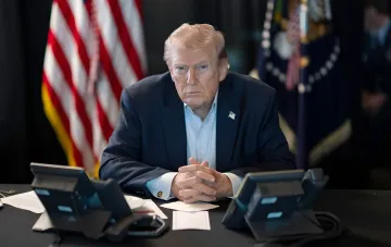 Дональд Трамп за столом з серйозним виразом обличчя, на фоні прапорів США — у контексті загрози потужного удару по Ірану після ракетної атаки