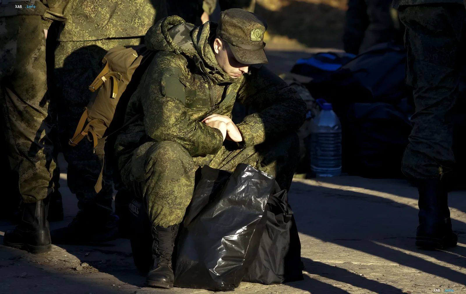 Уставший российский солдат в камуфляже сидит на земле с рюкзаком, символизируя человеческую цену войны и нагрузку на региональные бюджеты из-за новых выплат