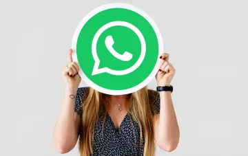 Женщина держит перед лицом логотип WhatsApp, символизируя переход к звонкам через браузер без установки приложения