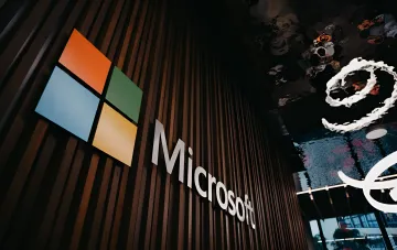 Логотип Microsoft на деревянной стене офиса, символизирующий запуск единого Copilot — суперприложения для чата, кода и агентов