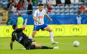 Игрок ФК «Динамо» в бело-голубой форме с логотипом GG dribbles the ball while being tackled by an opponent in a black kit during the Europa League match against PAOK in Thessaloniki.