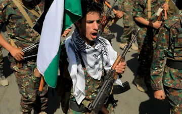 Huthi-Kämpfer mit Sturmgewehr und jemenitischer Flagge vor einer Gruppe bewaffneter Kämpfer in Tarnanzug