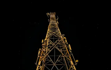 Высокая вышка сотовой связи ночью, символизирующая будущую сеть 6G, способную видеть сквозь стены