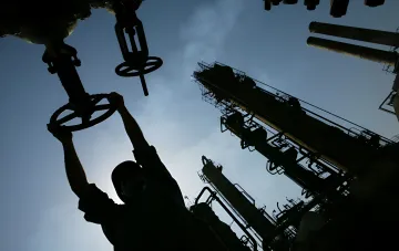 Силуэт рабочего на нефтеперерабатывающем заводе управляет вентилем на фоне промышленных труб и вышек