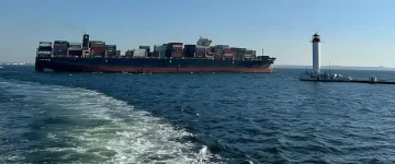 Грузовое судно с контейнерами в море рядом с маяком — символ остановки судоходства из украинских портов