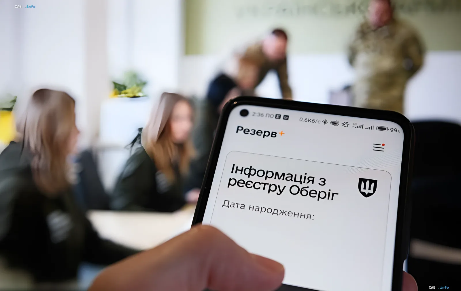 Смартфон с открытым приложением Резерв+ и информацией из реестра Оберіг на экране, на фоне люди в военной форме
