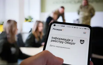 Смартфон с открытым приложением Резерв+ и информацией из реестра Оберіг на экране, на фоне люди в военной форме