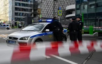 Полицейские у патрульного автомобиля на фоне поврежденного здания в Москве, иллюстрирующие усиление мер безопасности в регионе