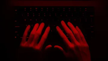 Hacker's hands on a keyboard in red light, symbolizing cyber threats of 2026