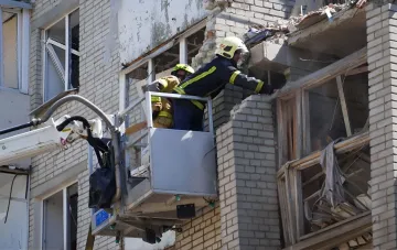 Пожарные спасатели на автовышке осматривают разрушенный фасад жилого дома после ракетной атаки в Львове