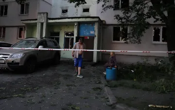 Folgen des ballistischen Anschlags in Kiew: beschädigtes Gebäude, zerstörtes Auto und Menschen hinter Absperrband