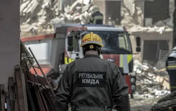 Спасатель КМДА в желтом шлеме осматривает разрушения после ночной атаки в Киеве