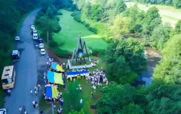 Luftaufnahme des Lagers „Artek Zakarpattien“: Kinder und Erwachsene mit ukrainischen Flaggen nahe einem Denkmal, neben einem Fluss und Straße mit Bussen — Kontrast zwischen festlicher Atmosphäre und berichteten schrecklichen Bedingungen von Unsauberkeit und Schimmel
