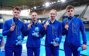 Украинские прыгуны в воду с медалями и плюшевыми игрушками на фоне бассейна после победы на ЧЕ в Париже