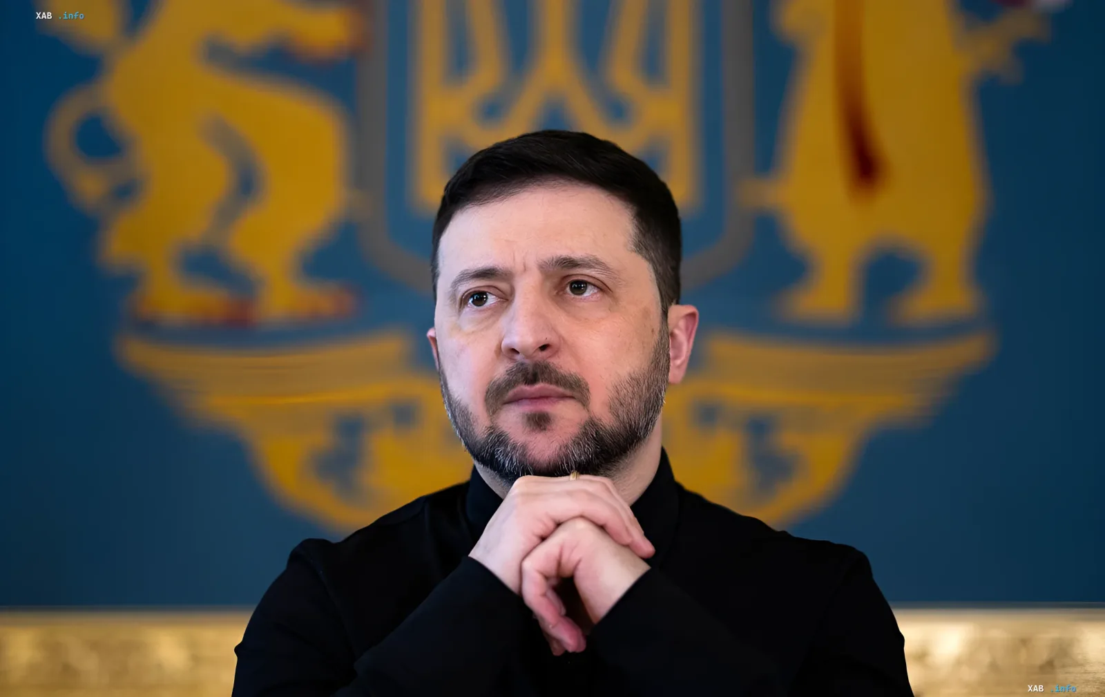 Президент Украины Владимир Зеленский задумчиво смотрит в сторону, на фоне герба Украины, обсуждая причины прорыва баллистической ракеты в Киев