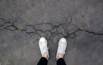 Risse im Asphalt vor weißen Turnschuhen — visuelle Metapher der Folgen des Erdbebens der Stärke 4,7 in Pozzuoli