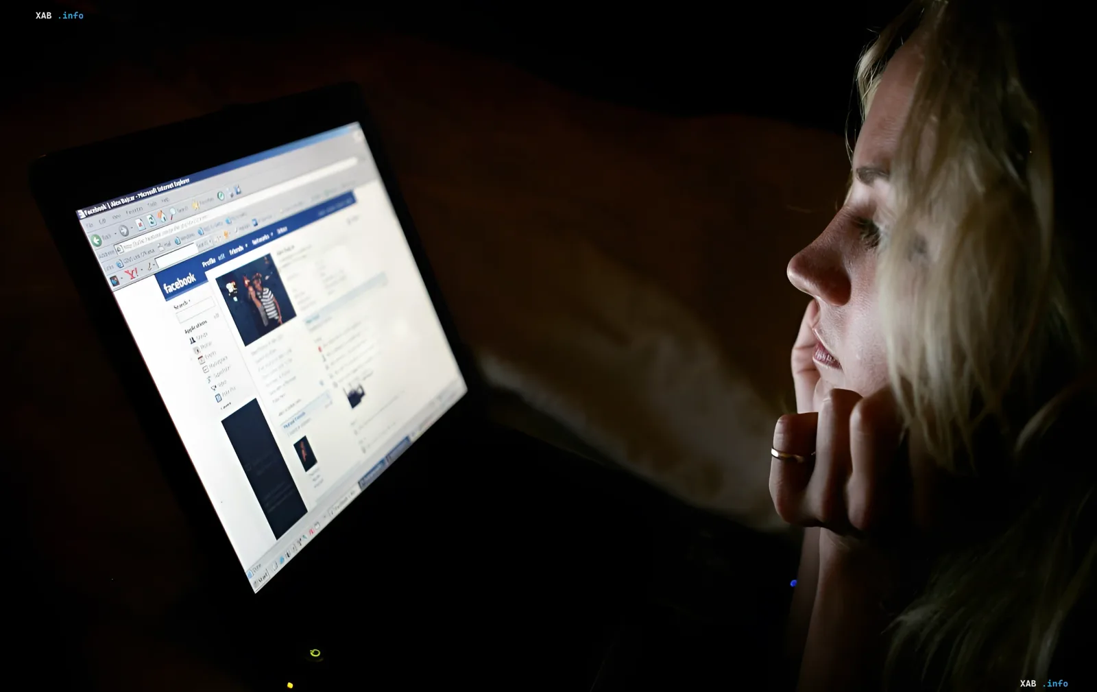 Teenager im Dunkeln starrt auf einen Laptop-Bildschirm mit Facebook, symbolisiert digitale Abhängigkeit und psychische Gesundheitsrisiken