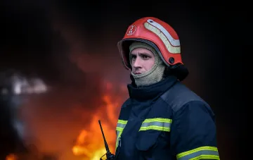 Firefighter in protective gear against the backdrop of fire after Russian drone attack on postal terminal in Kharkiv
