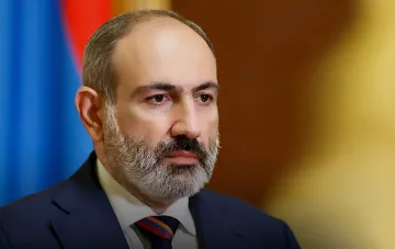 Ніколь Пашинян у моменті оголошення про відставку на фоні прапора Вірменії