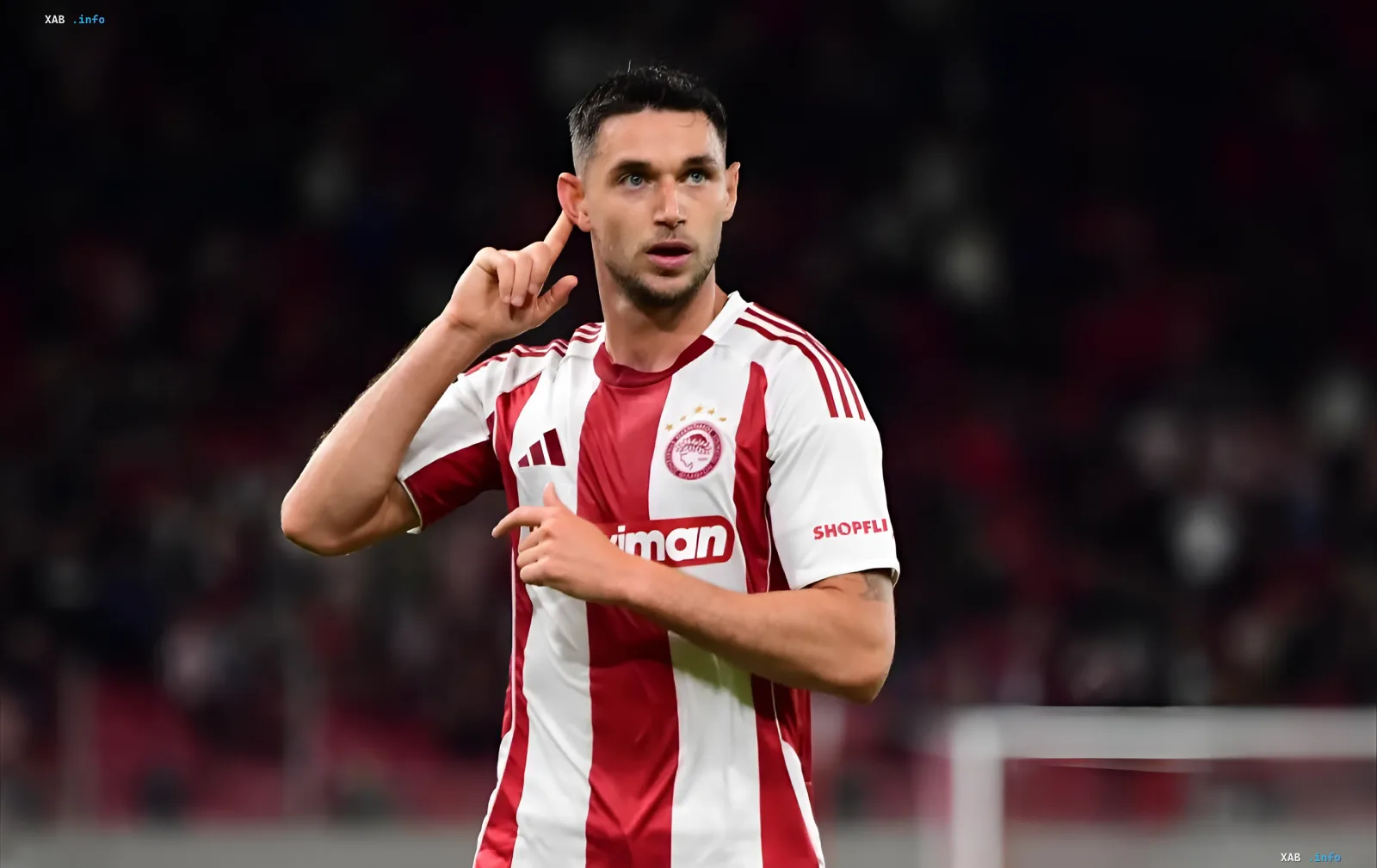 Roman Yaremchuk in Olympiacos kit making a 'thinking' gesture — possibly hinting at tactical error or exclusion from Champions League squad