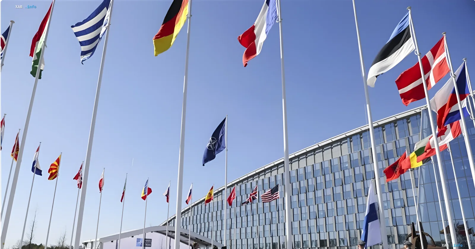 Flags of NATO member countries, including the US and Germany, waving in front of the alliance's headquarters in Brussels, symbolizing the transfer of responsibility for Ukraine's security program from the US to NATO