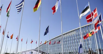 Flags of NATO member countries, including the US and Germany, waving in front of the alliance's headquarters in Brussels, symbolizing the transfer of responsibility for Ukraine's security program from the US to NATO