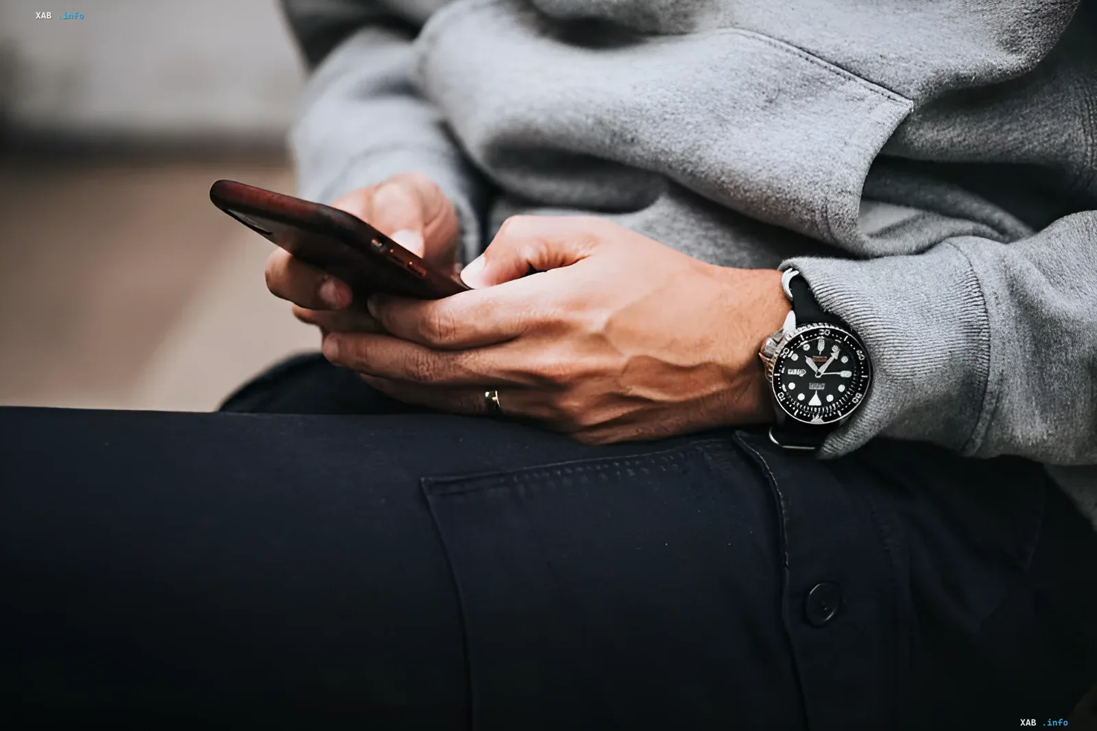 Person in grauem Hoodie hält Smartphone, symbolisiert Nutzung von Pflicht-Apps einschließlich Alice AI, vom russischen Staat bis 2027 genehmigt
