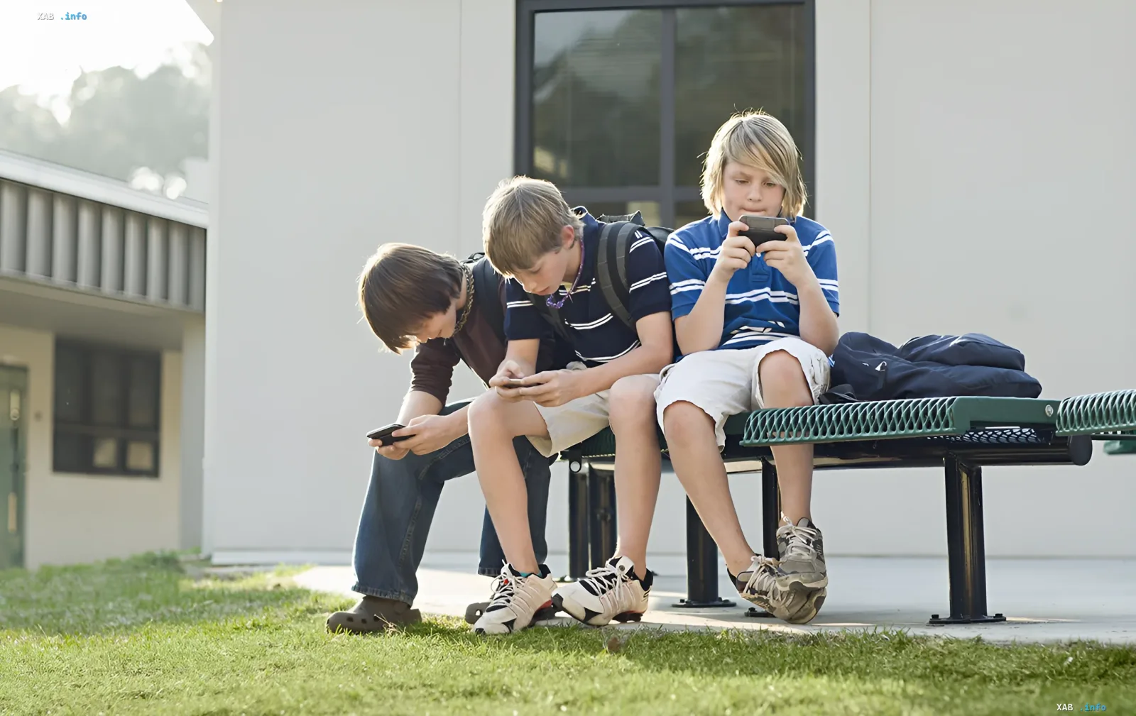 Three schoolboys sitting on a bench engrossed in their smartphones, illustrating the topic of cyber risks among teenagers
