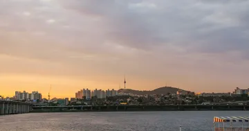 Панорама Сеула на закате: вид на реку Хан, мосты и телебашню N Seoul Tower на фоне оранжевого неба — символ экстремальной жары в Южной Корее