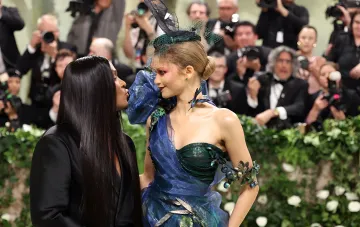 Star in an extravagant blue-green dress with feathers and a net on her head, created by a stylist, posing on the red carpet in front of photographers