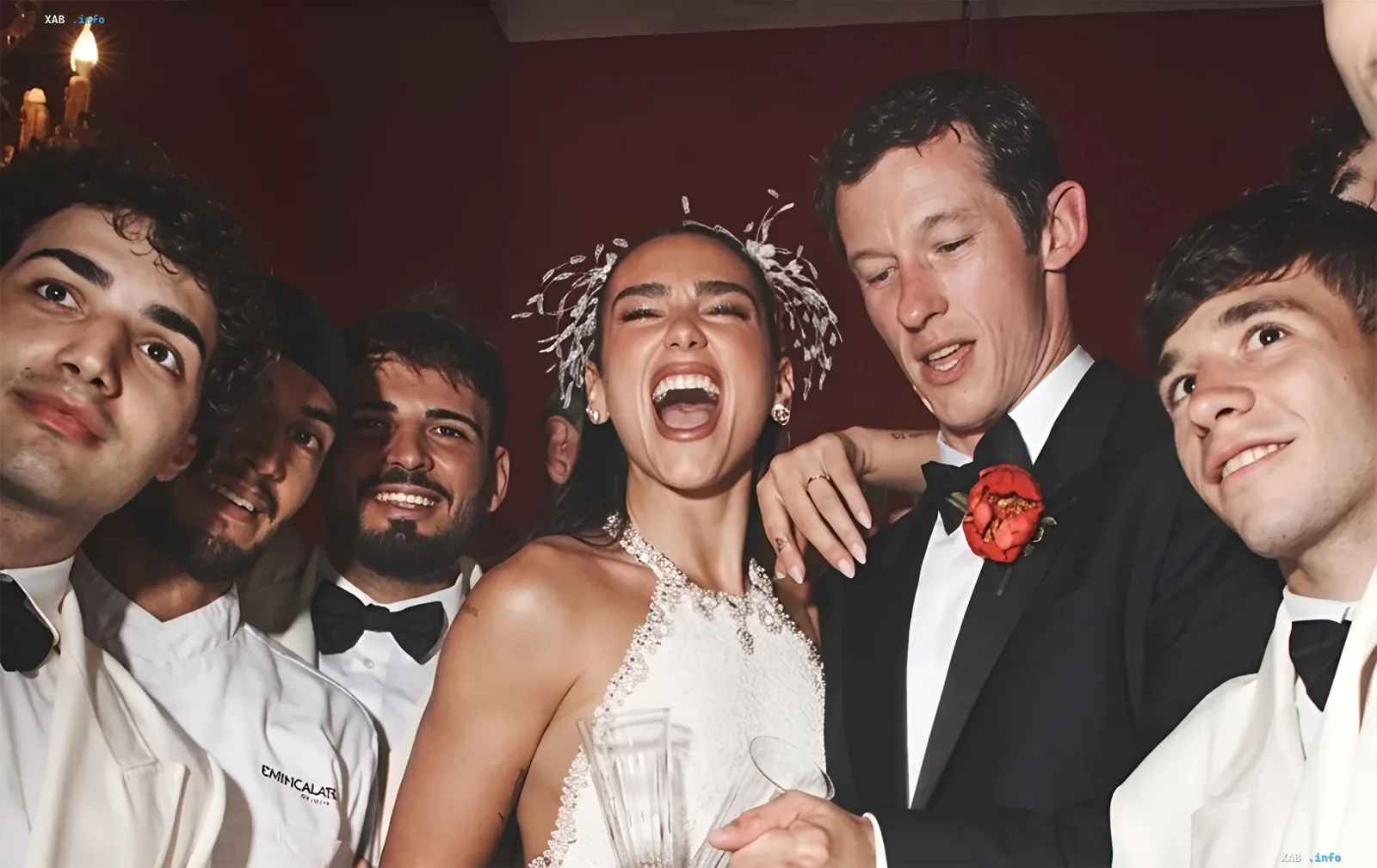 Dua Lipa in a crystal-embellished wedding dress with an unconventional feather tiara, surrounded by guests in tuxedos — a bold example of 2026 wedding fashion