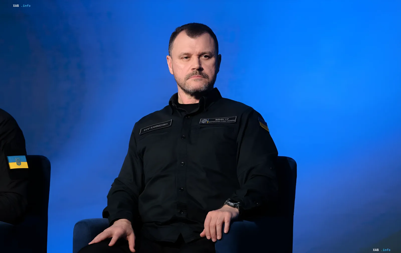 Игорь Клименко в черной форме с украинским флагом на фоне синего экрана, символизирующий его новую роль в СНБО
