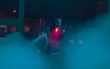 Person in futuristischen Nachtsichtbrillen mit Vollfarbdisplay, beleuchtet von rotem Licht, vor einem rauchigen neonbeleuchteten Innenraum