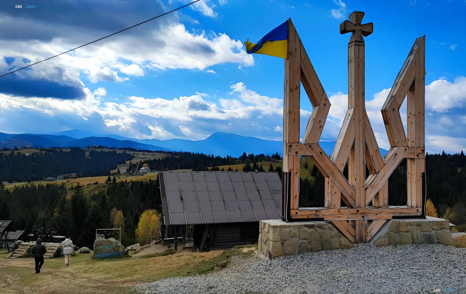 Украинский флаг развевается на фоне горного пейзажа у деревянного тризуба, символизируя выбор безопасного отдыха в горах Украины этим летом