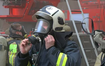 Feuerwehrmann in Schutzausrüstung und Sauerstoffmaske am Ort eines Brandes am BSTU Schukow nach einem Drohnenangriff
