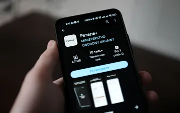 Smartphone mit geöffnetem Reserv+-App im Google Play, illustriert die Nachricht über Ausfall des Dienstes und Widerlegung durch das ukrainische Verteidigungsministerium