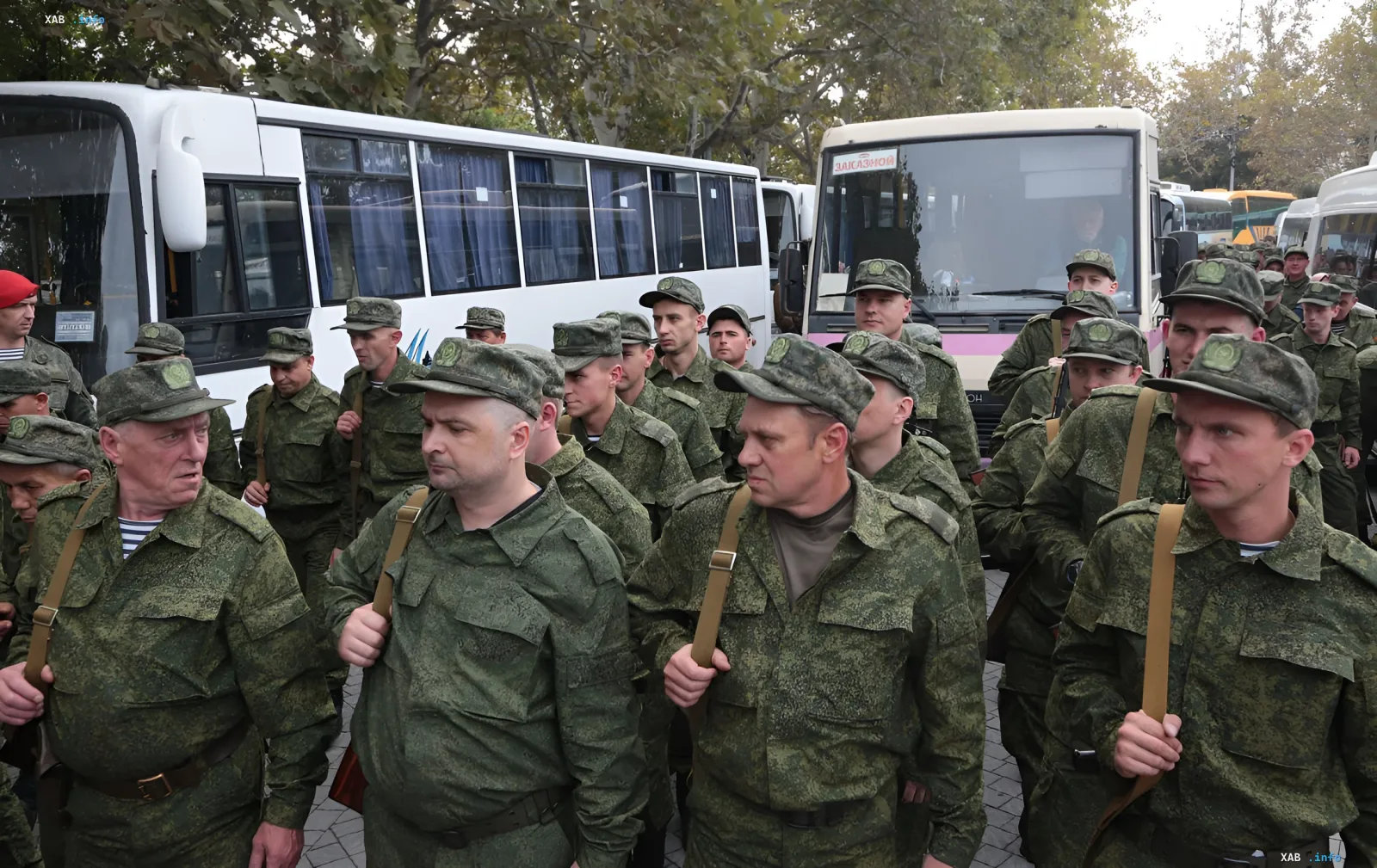 Группа российских военных в камуфляжной форме и фуражках с эмблемами стоит у автобусов, что иллюстрирует тему вербовки и мобилизации на фоне кризиса