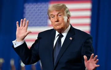 Дональд Трамп на фоне флага США жестикулирует, символизируя отмену удара по Ирану и начало переговоров